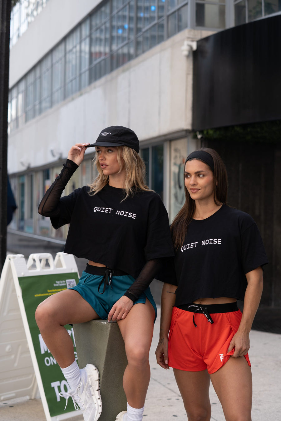 Two women outdoors in black Quiet Noise Crop tops, one wearing a cap.