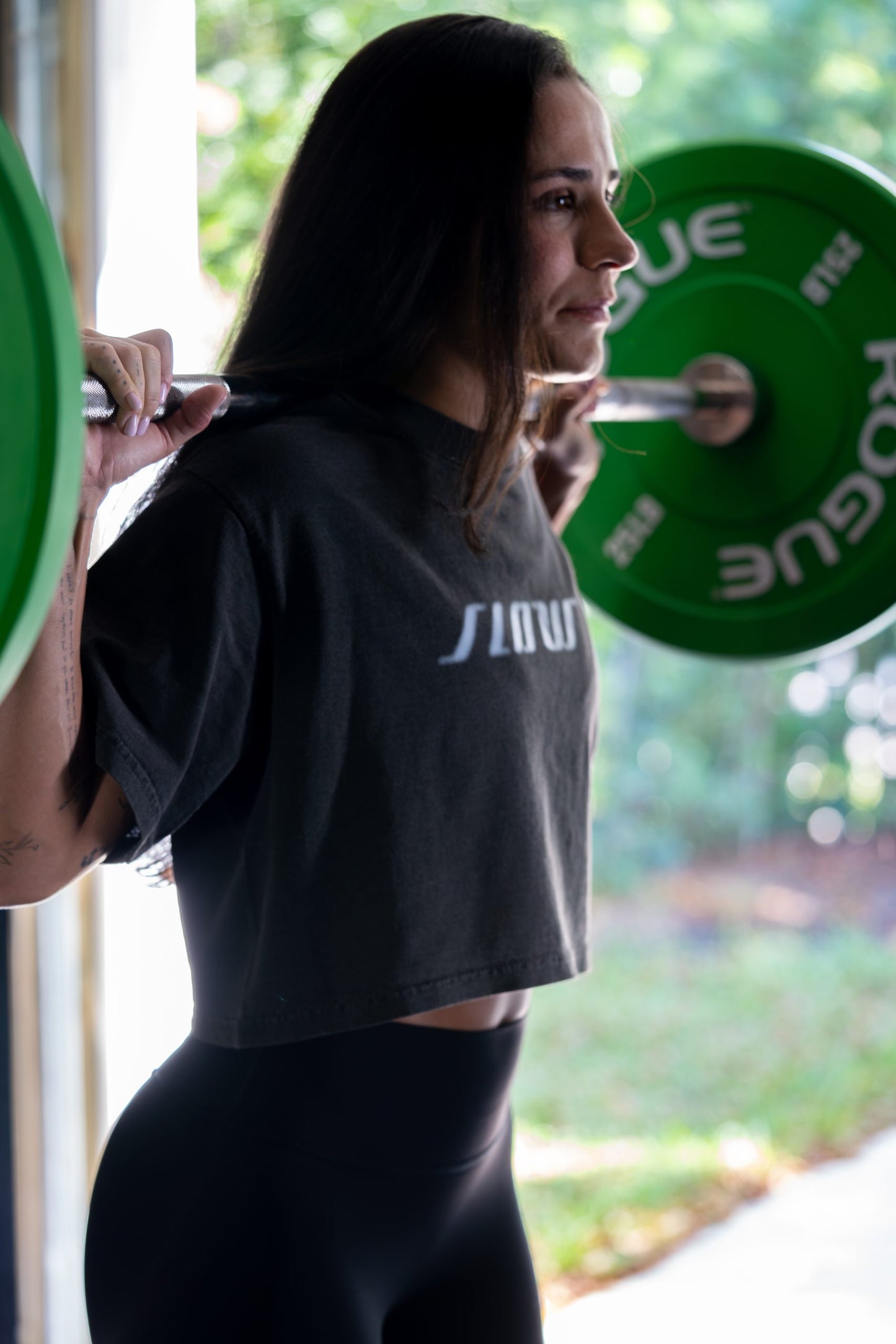 A woman racking a barbell, seen from behind in the charcoal Slow Crop.