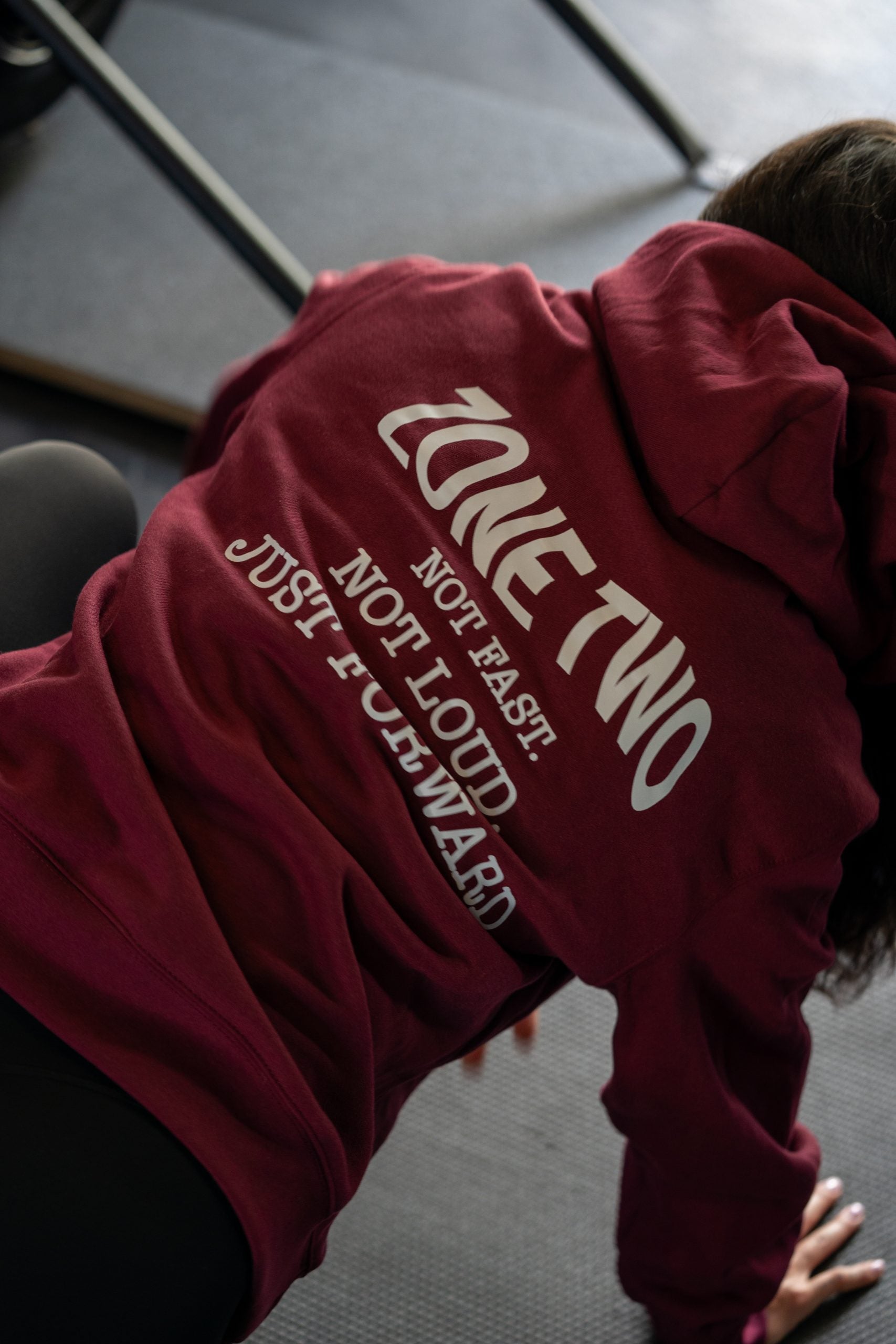 Close-up of the back of the burgundy Forward Hoodie, arced ZONE TWO — NOT FAST. NOT LOUD. JUST FORWARD.