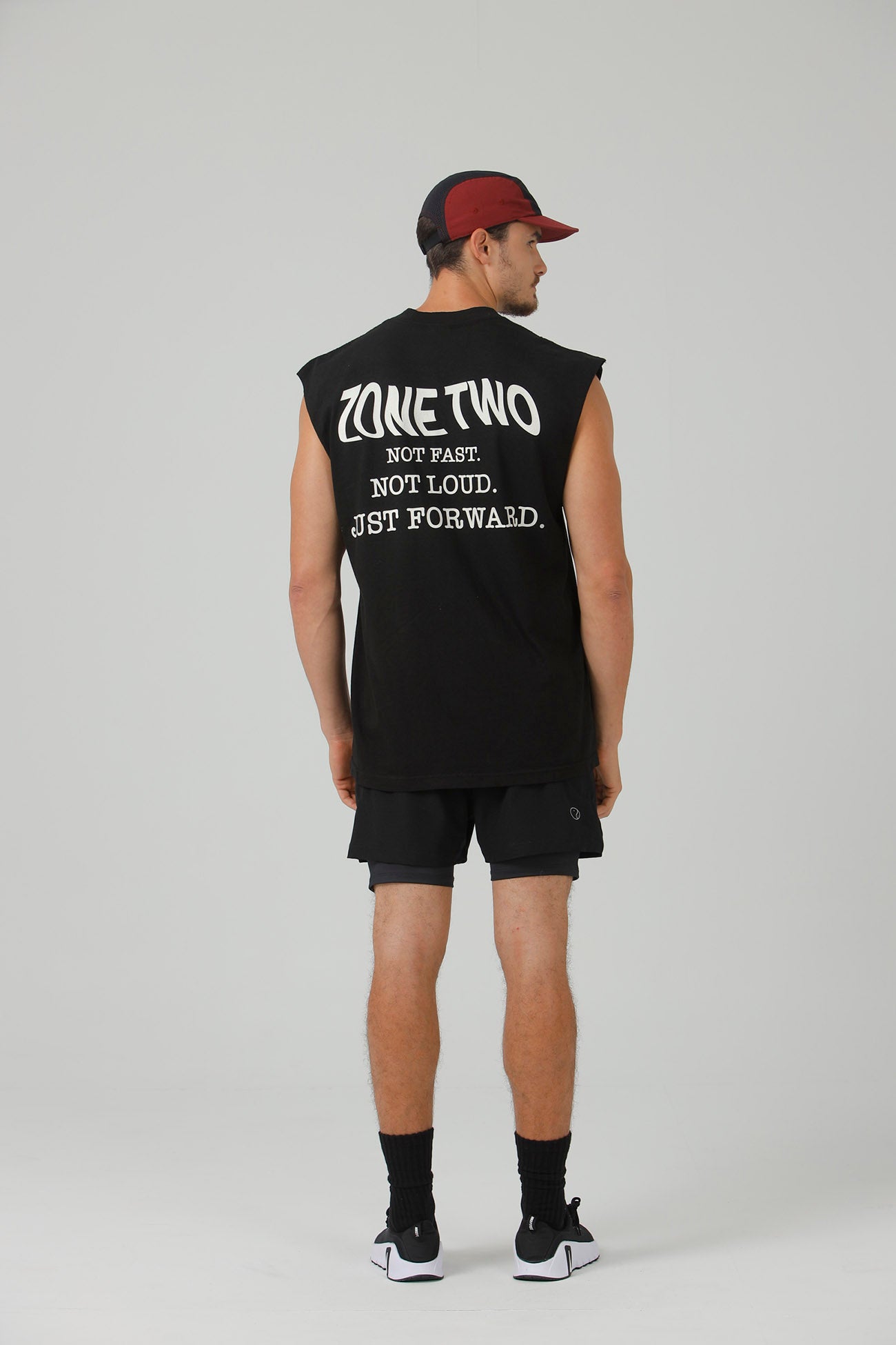 A man seen from behind in the black Forward Tank and a burgundy cap, showing the back print.