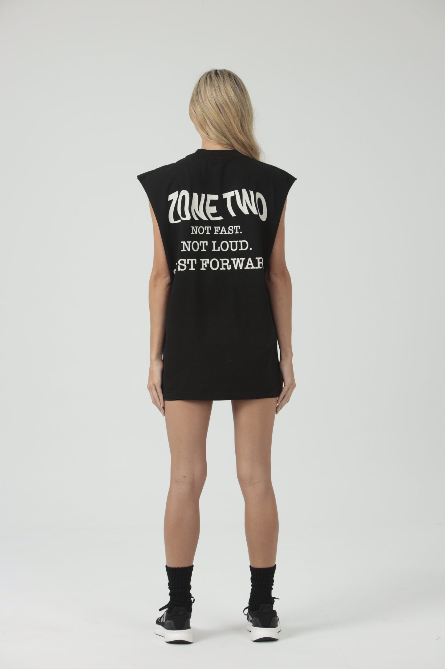 A model seen from behind in the black Forward Tank, printed ZONE TWO — NOT FAST. NOT LOUD. JUST FORWARD.