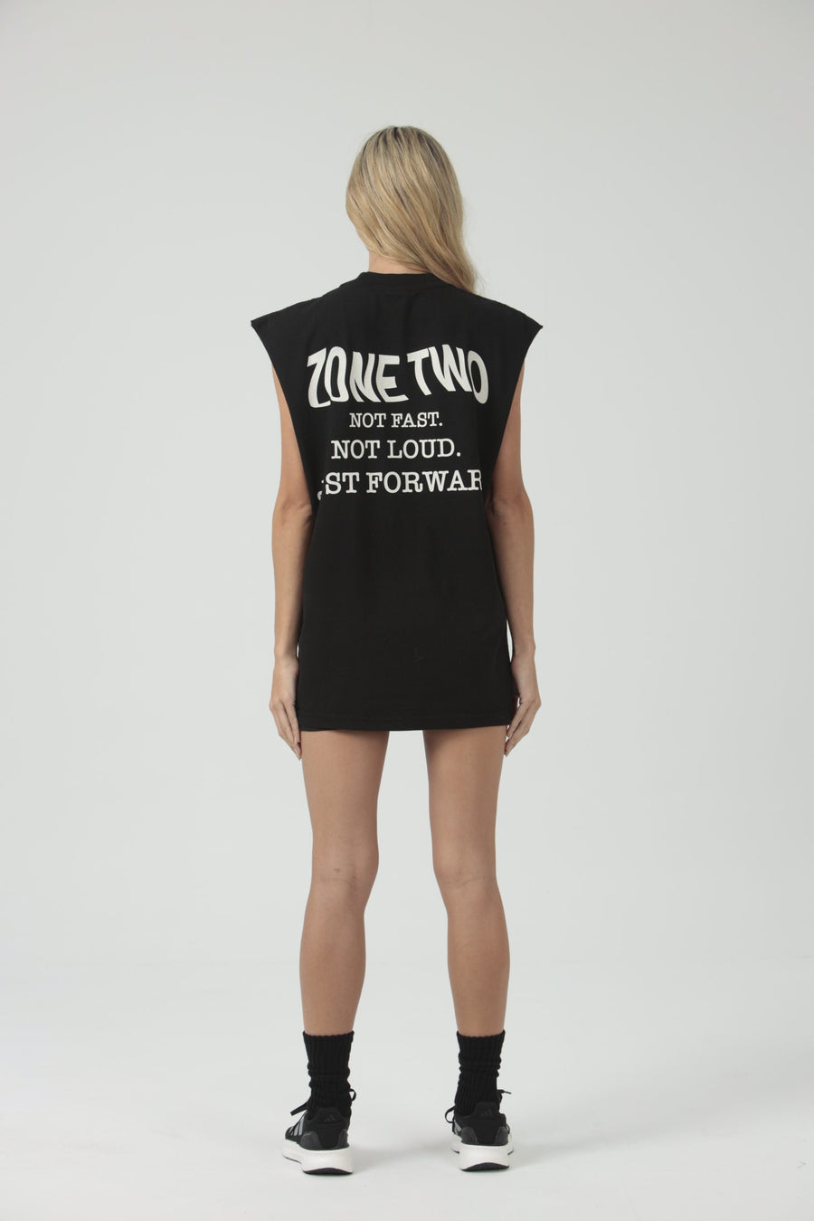 A model seen from behind in the black Forward Tank, printed ZONE TWO — NOT FAST. NOT LOUD. JUST FORWARD.