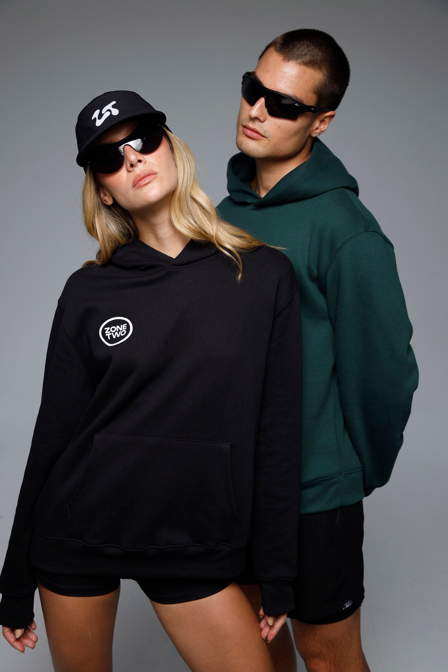 Two models in the Quiet Hoodie, one in black with a cap and one in green.