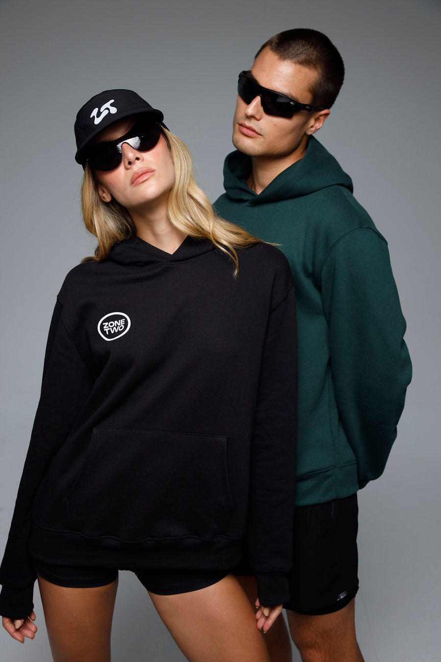 Two models in the Quiet Hoodie, one in black with a cap and one in green.