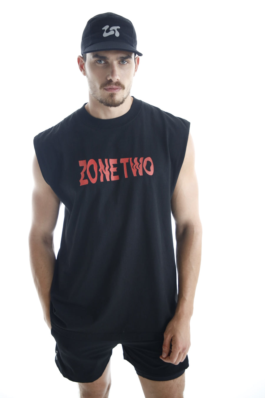 A man wearing the Axis Tank, a dark sleeveless top with ZONE TWO printed in red across the chest, and a cap.