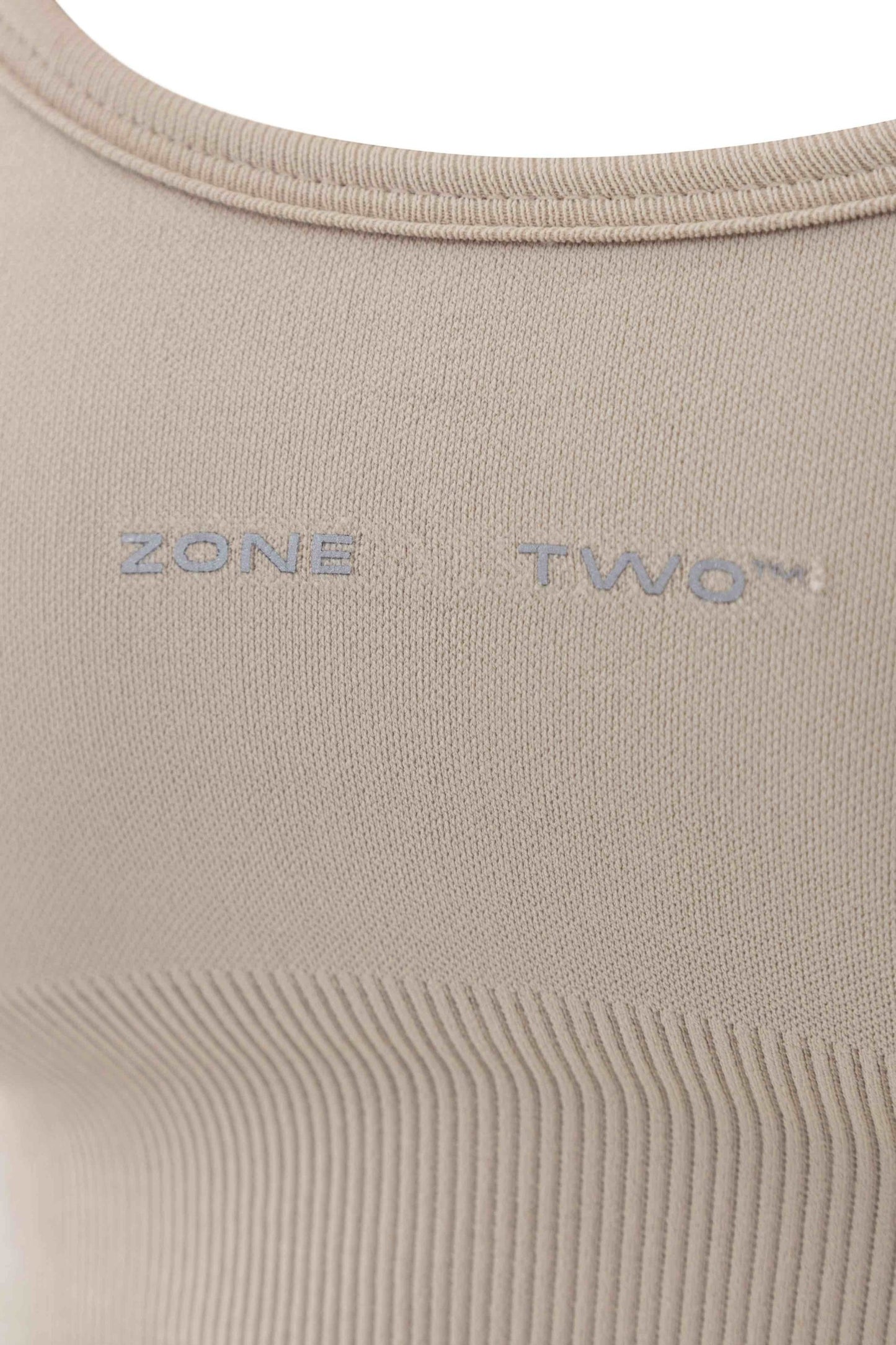 Close-up of the beige Top Flow Racerback showing the Zone Two wordmark and ribbed underband.