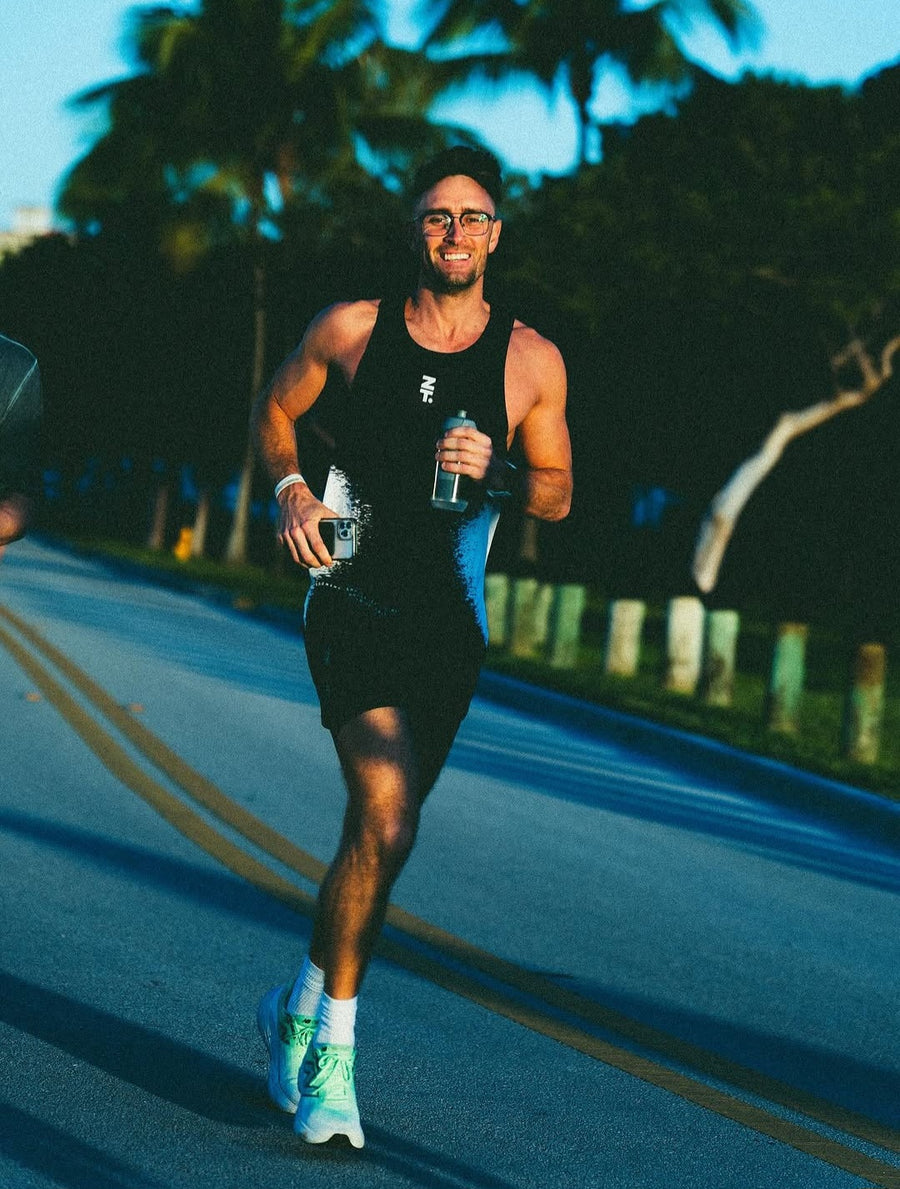 A runner on a road holding a bottle, wearing a dark Static Tank.